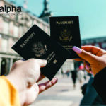 como solicitar o Green Card americano? (Na imagem tem duas mãos, cada uma segura um passaporte americano. No canto superior direito, tem a logo da Alpha Language Consulting).